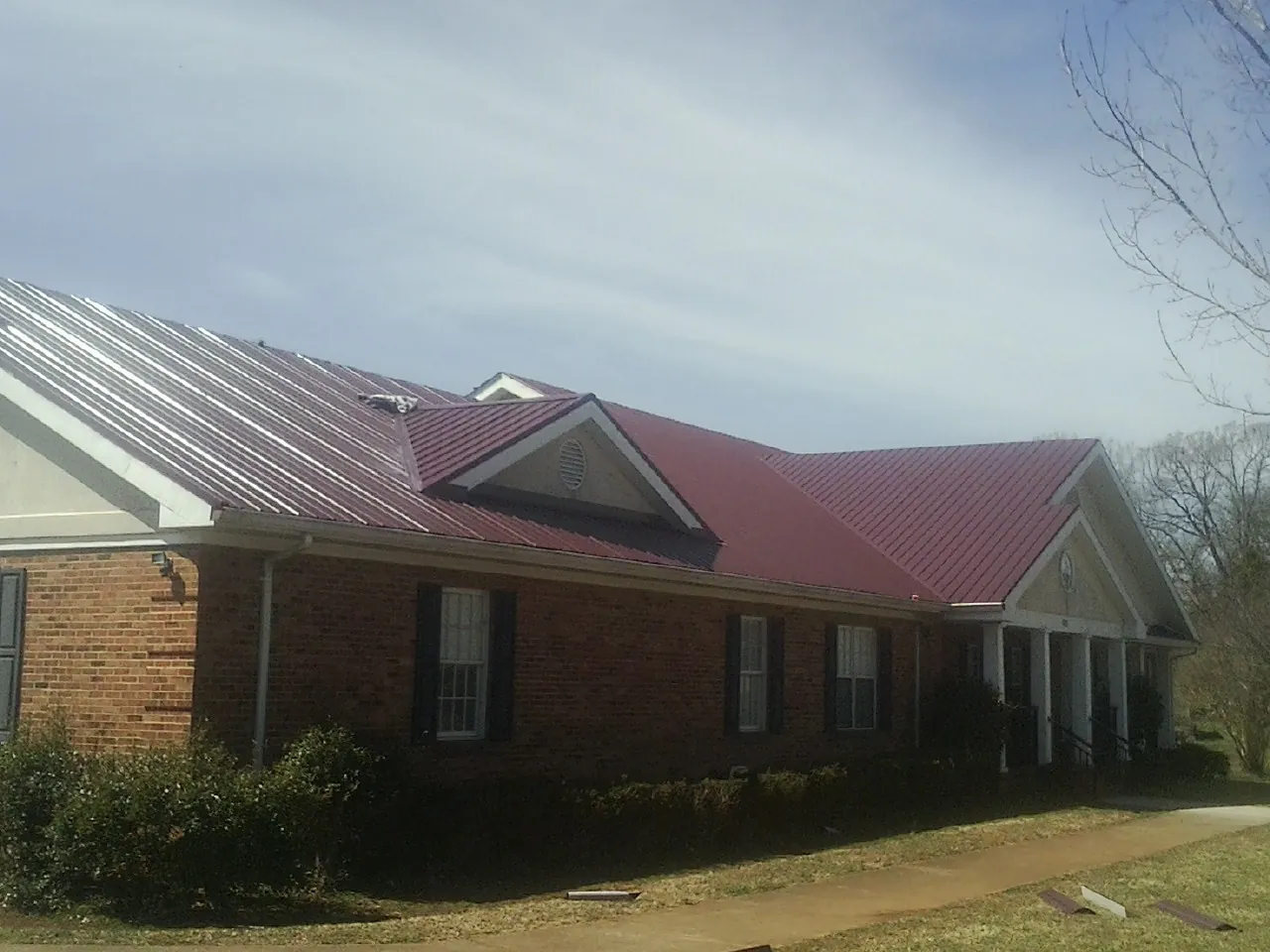 Red metal roof with gabled entries on a long brick building, from a Hail Damage Roof Repair job in Lyons